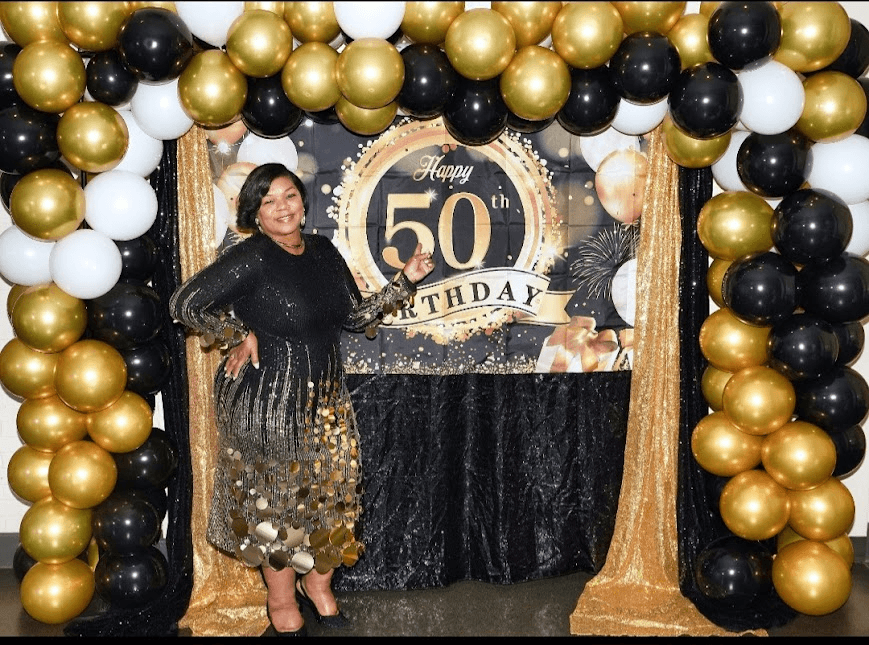 Birthday photography: woman in a black and gold sequin dress beside a 50th birthday backdrop and balloon arch