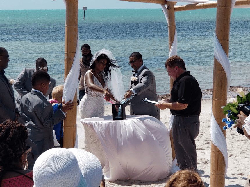 Wedding photography: bride and groom performing a sand ceremony under a bamboo arch on the beach