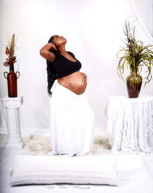 Maternity portrait: expecting mother in a black top and white skirt posing in a white studio set