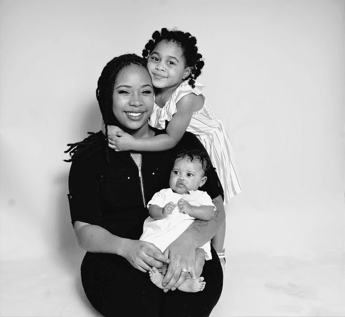 Black and white studio portrait of a mother holding her baby while her daughter hugs her from behind